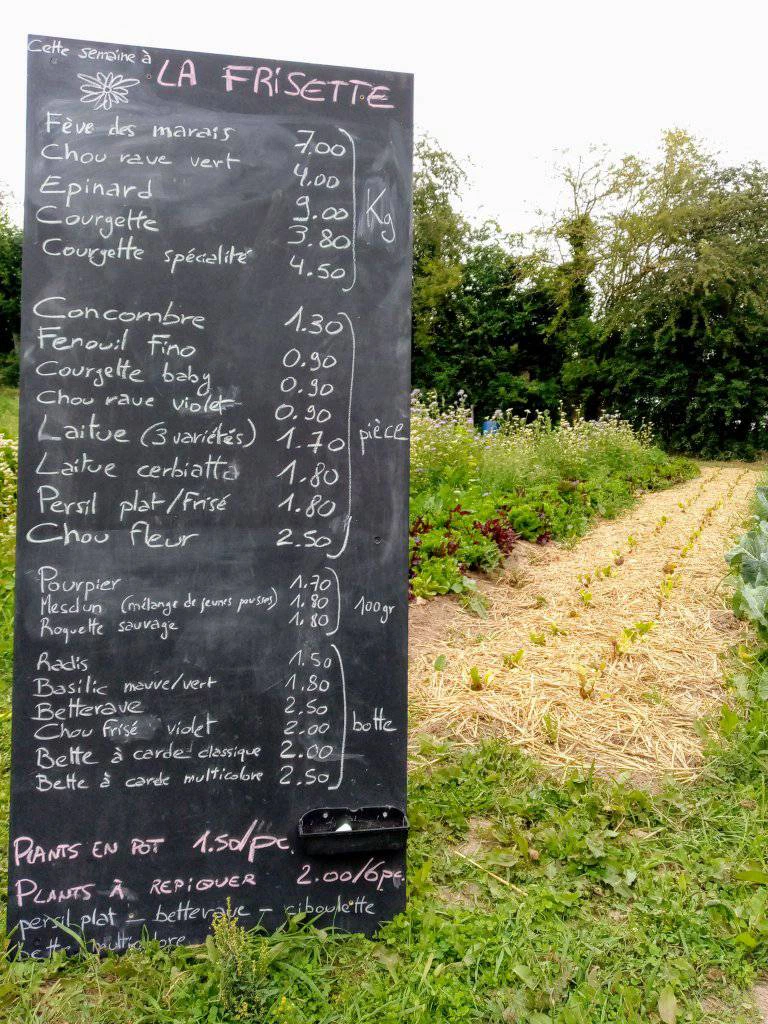 Un tableau affichant la liste des prix des légumes frais à côté d'un champ cultivé à Blarégnies, sous l'enseigne 