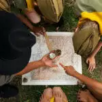 Groupe d'enfants en tenue de scout rassemblés autour d'une carte au sol, utilisant une boussole pour s'orienter dans Blarégnies.